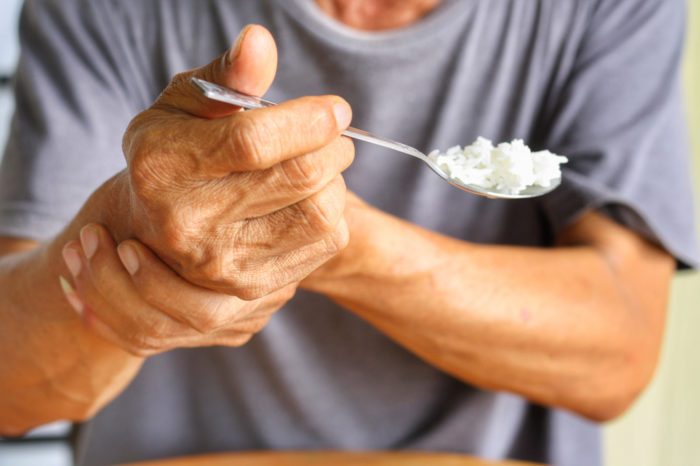 white man struggling to eat by holding shaking wrist representing cbd and parkinsons
