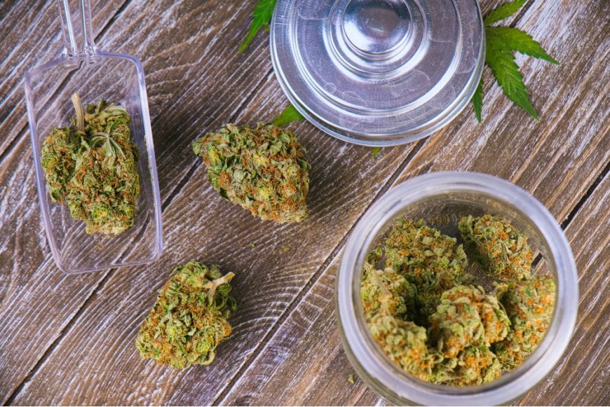cannabis buds inside glass jar and sitting on wood plank