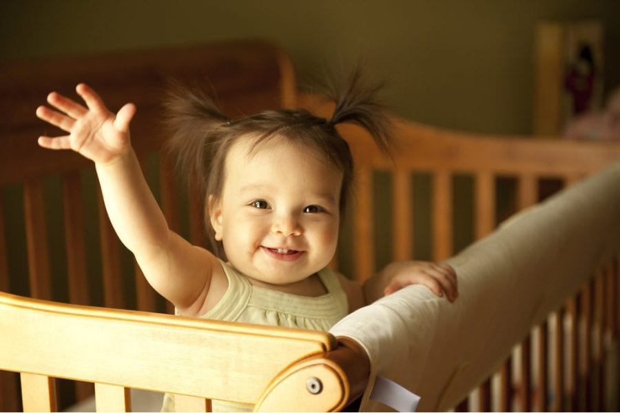 Happy baby waving from crib