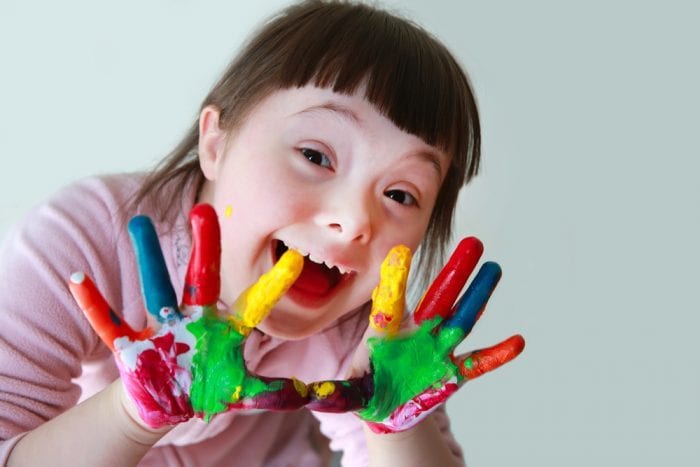 Happy child with Trisomy 21 holding up painted hands