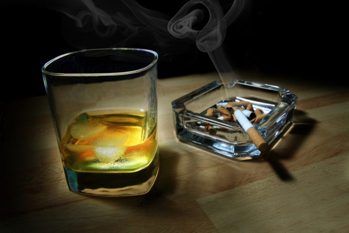 scotch beside ashtray with smoking cigarette